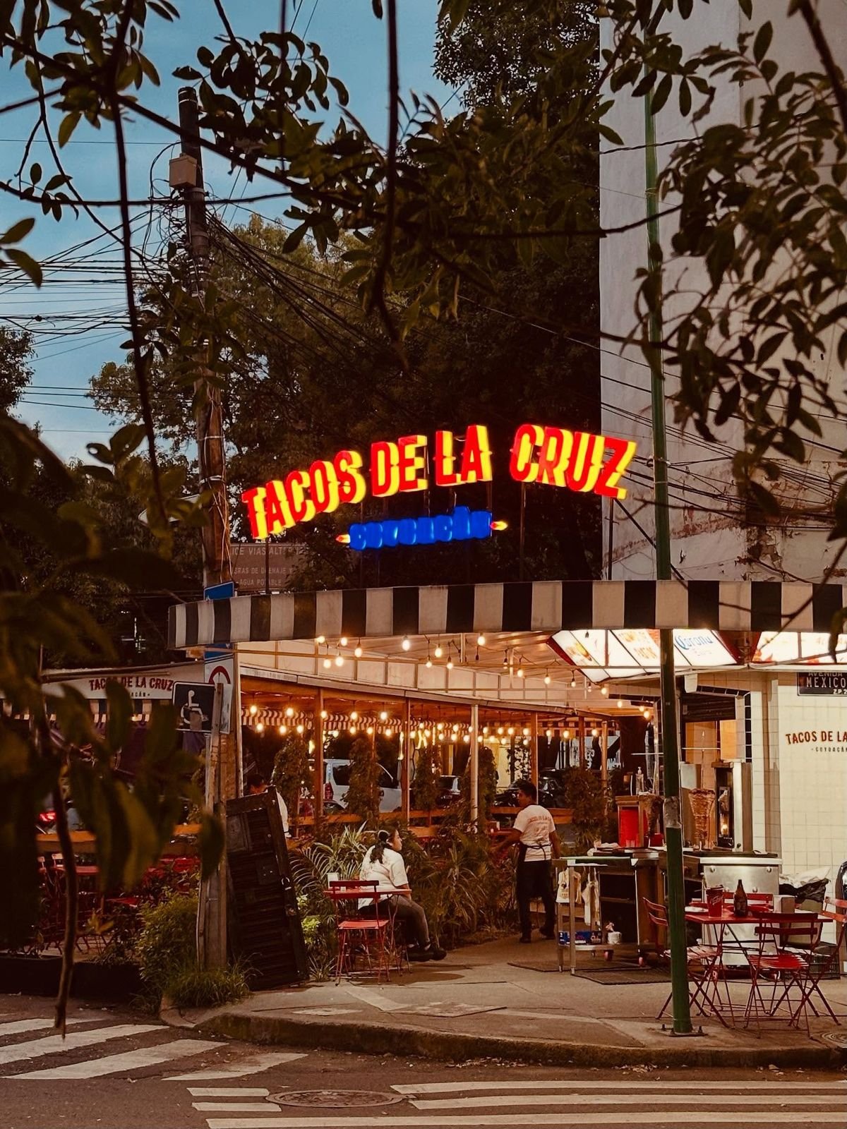 Letrero luminoso de Tacos de la Cruz sobre la terraza al anochecer