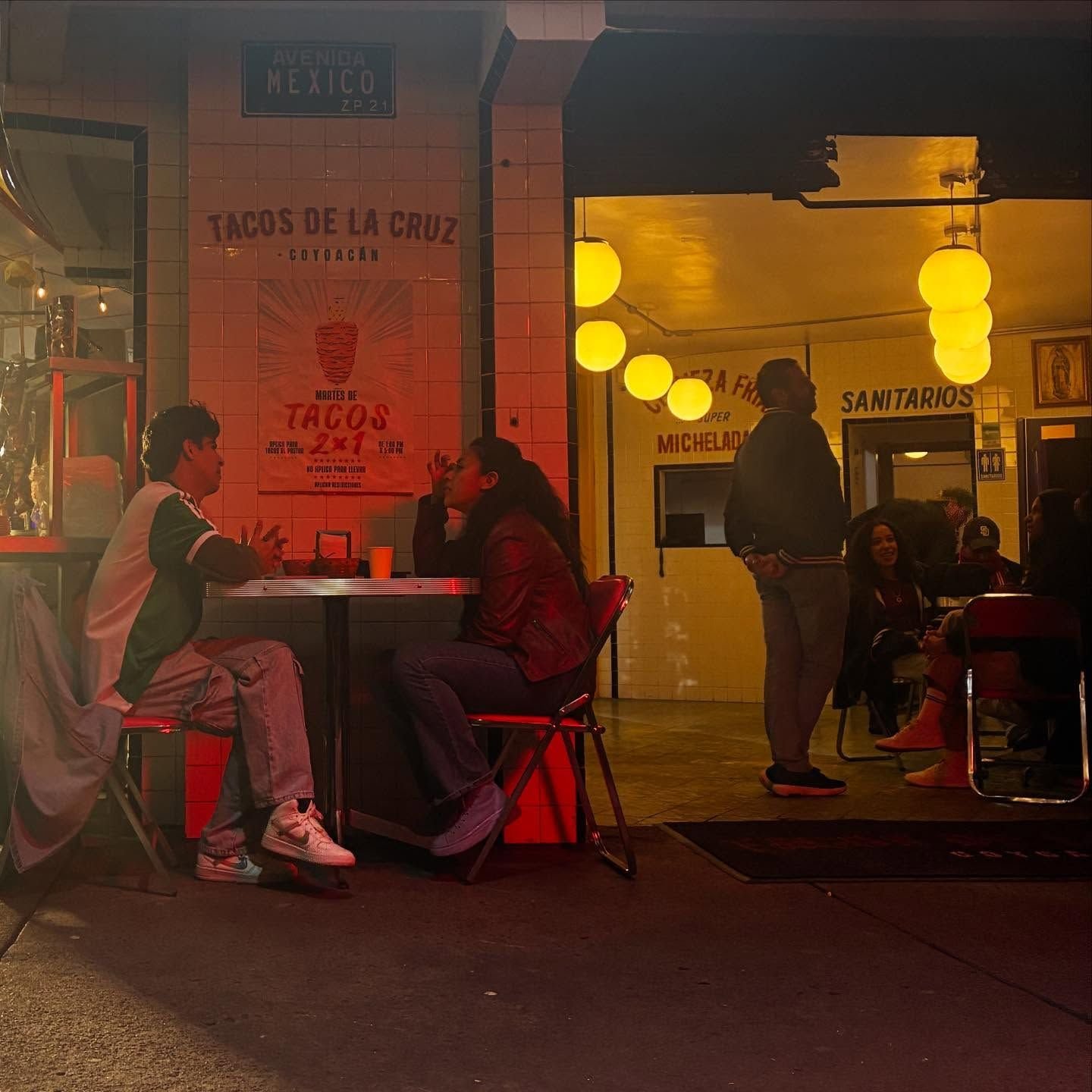 Comensales de noche junto al muro de azulejo y la entrada iluminada