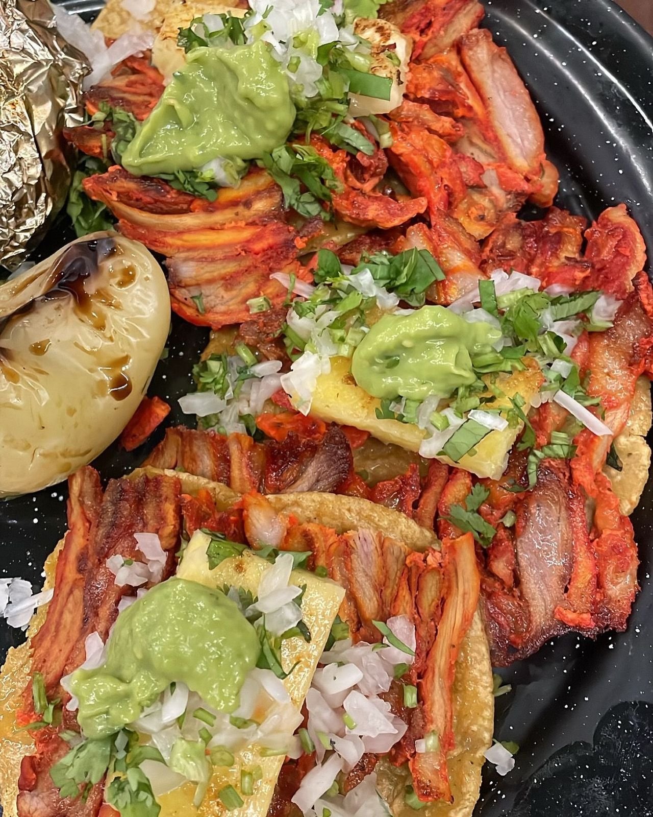 Plato de tacos de trompo con guacamole y cebolla asada