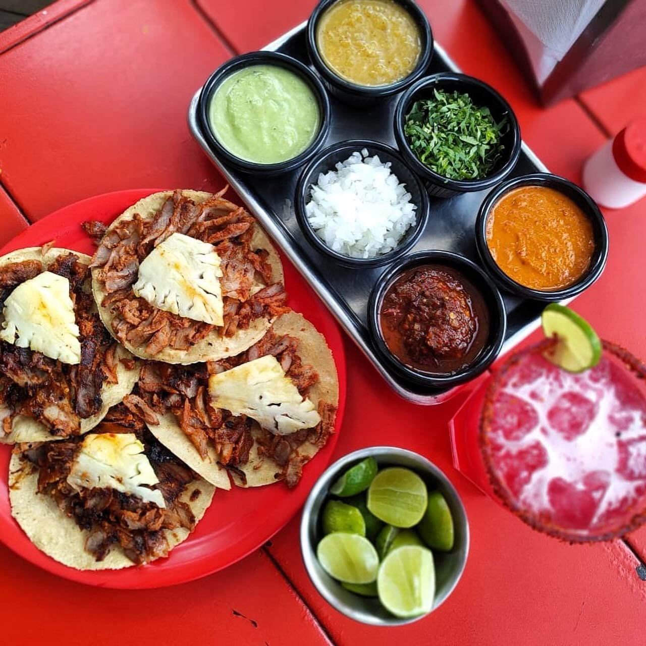 Tacos al pastor, charola de salsas, limones y michelada vista desde arriba