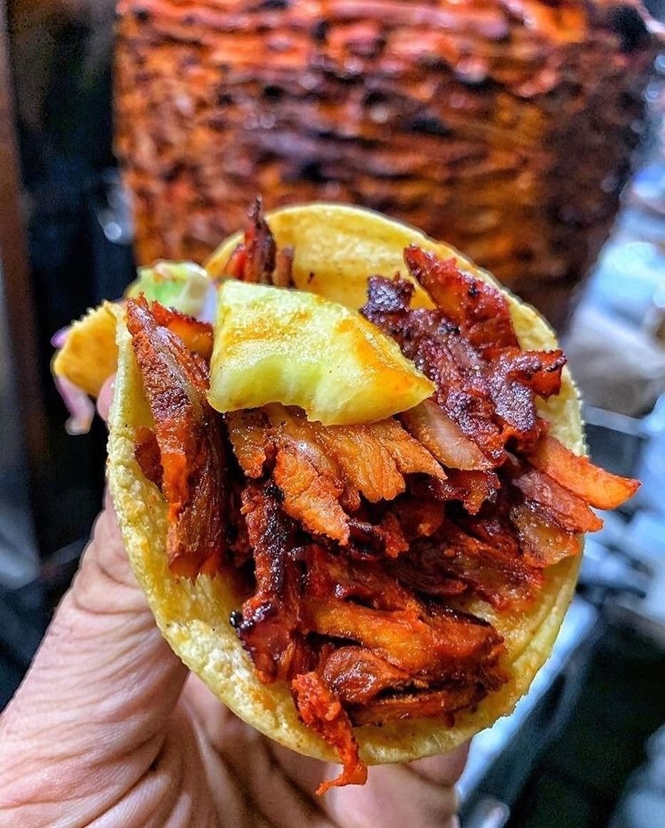 Taco al pastor con piña frente al trompo